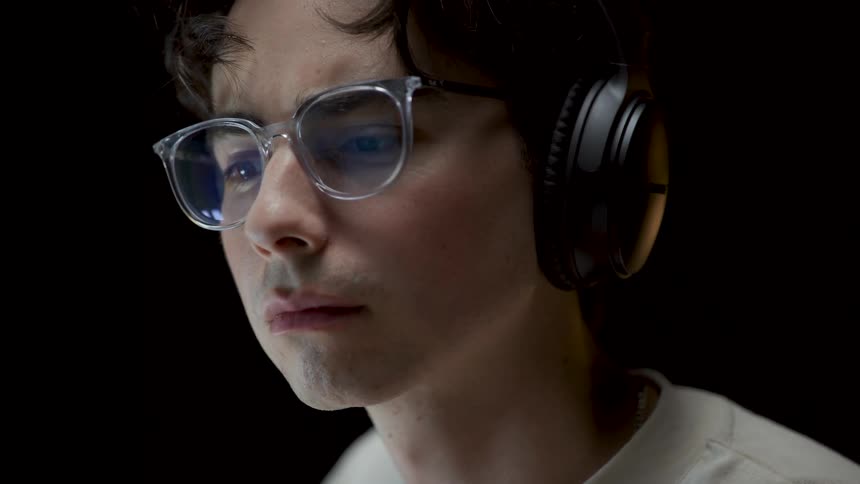 Man with headphones and glasses glances down and squints