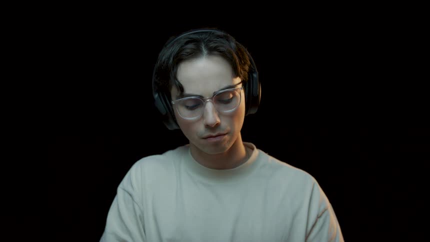 Man with glasses headphones and white t shirt works on computer in studio