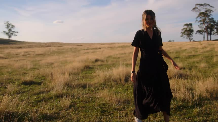 A woman wearing a black dress and sneakers walks in an open field