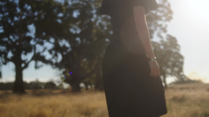 Woman in long black dress walking through a pasture on a sunny day