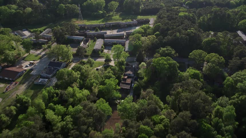 Approaching abandoned buildings among trees in West Atlanta during a sunny day captured in aerial stock footage