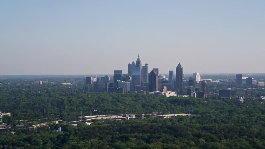 A distant and sunny aerial view of Midtown Atlanta skyscrapers rising above trees in Buckhead Georgia during the daytime
