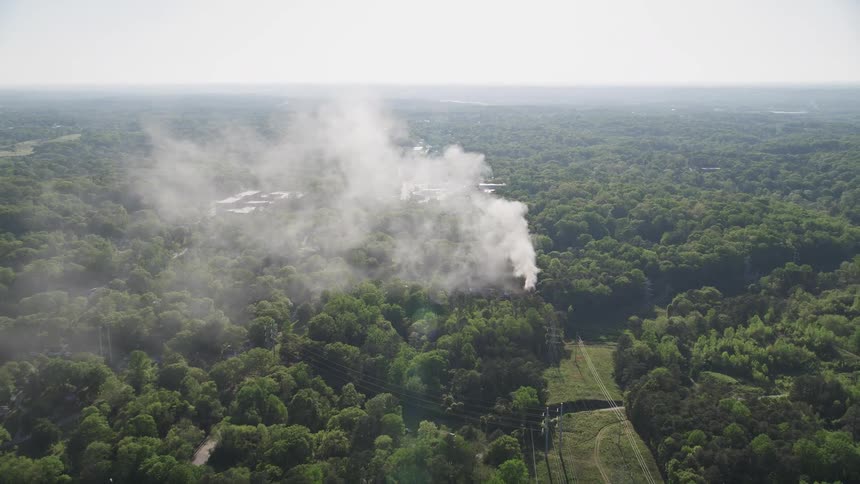 Aerial footage of a house fire in a wooded area with smoke rising and tilt to get a birds eye view of the scene in West Atlanta Georgia