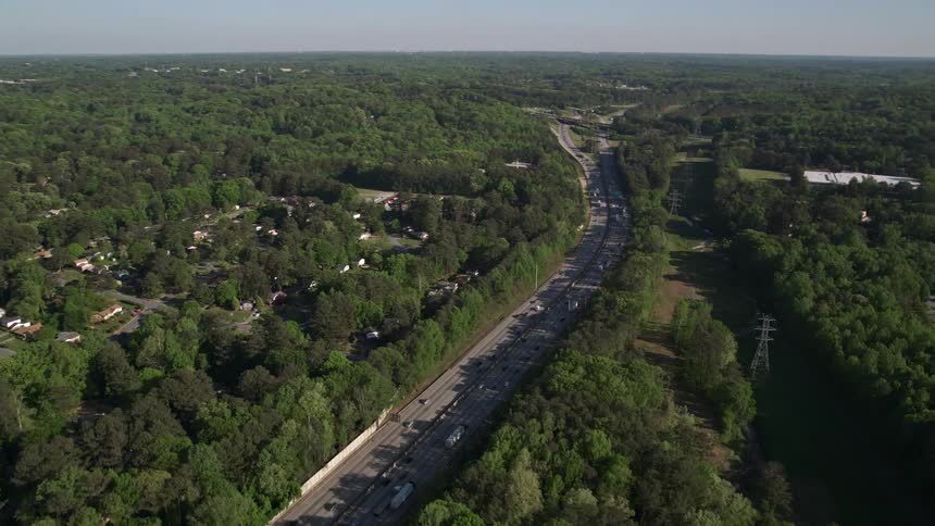 Aerial footage of heavy traffic on a West Atlanta interstate surrounded by trees during daytime