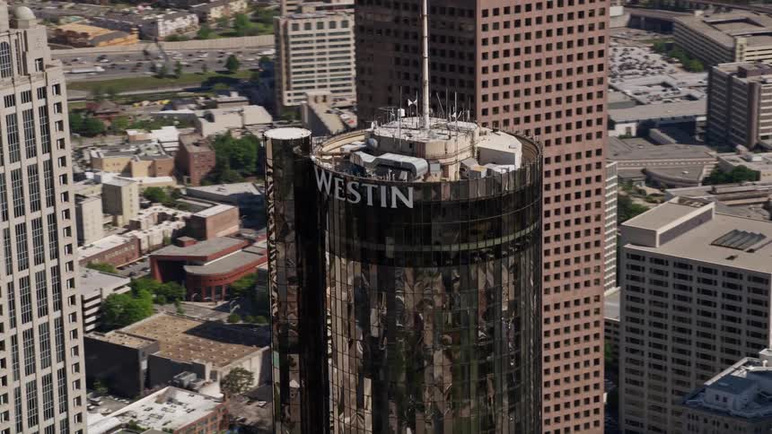 An aerial stock footage of Westin Peachtree Plaza Hotel orbiting on top showing a high-rise building standing in downtown Atlanta with heavy traffic flowing along the highway in the background