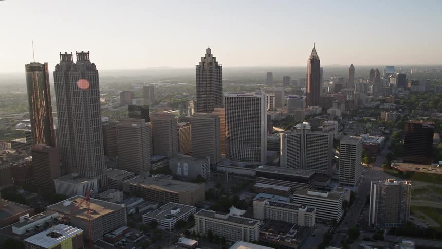 Approaching downtown Atlanta at sunset this aerial footage shows a hazy skyline of high-rise buildings including the Bank of America Plaza the Westin Peachtree Plaza Hotel and the SunTrust Plaza Tower