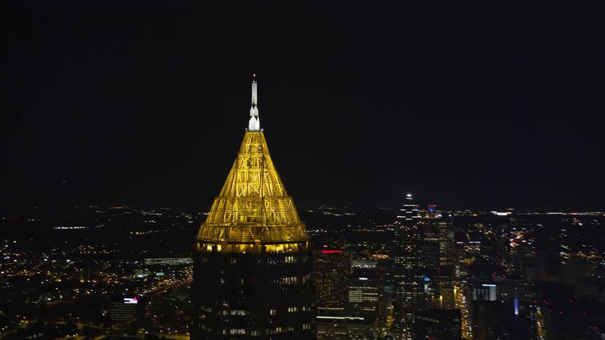 An aerial footage shows Bank of America Plaza a tall skyscraper towering over Atlanta at night with a pyramid-shaped structure illuminated on top