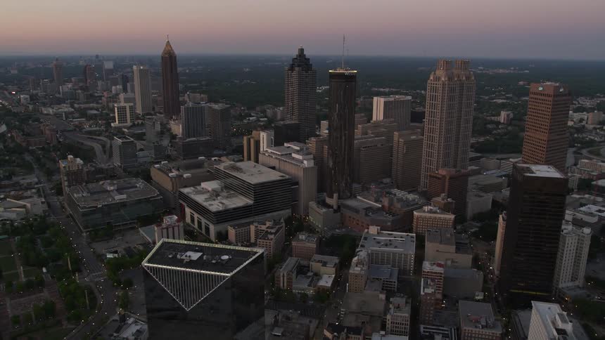 An aerial view of Downtown Atlanta at twilight flying towards the Westin Peachtree Plaza Hotel and capturing the towering skyscrapers and hazy cityscape