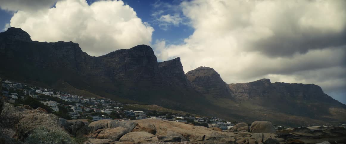 Houses are along a mountain hillside and in the valley as cumulus clouds move across the sky