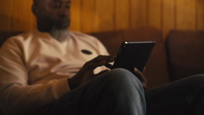 Older man sits on couch scrolling on tablet