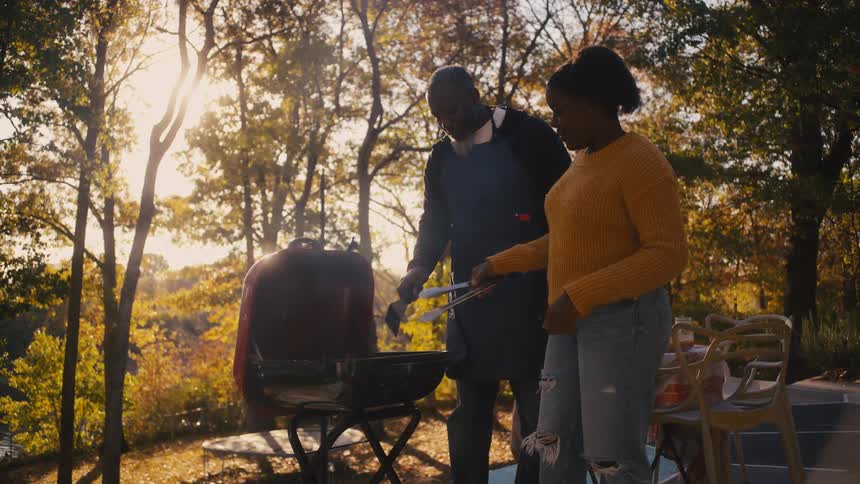 A father and teenage daughter cooking food on an outdoor grill in autumn