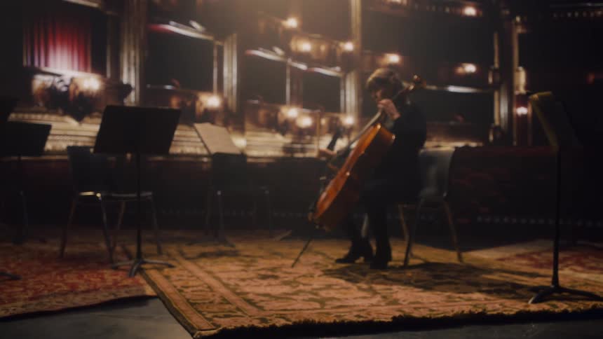 A woman is sitting in an empty room playing a cello