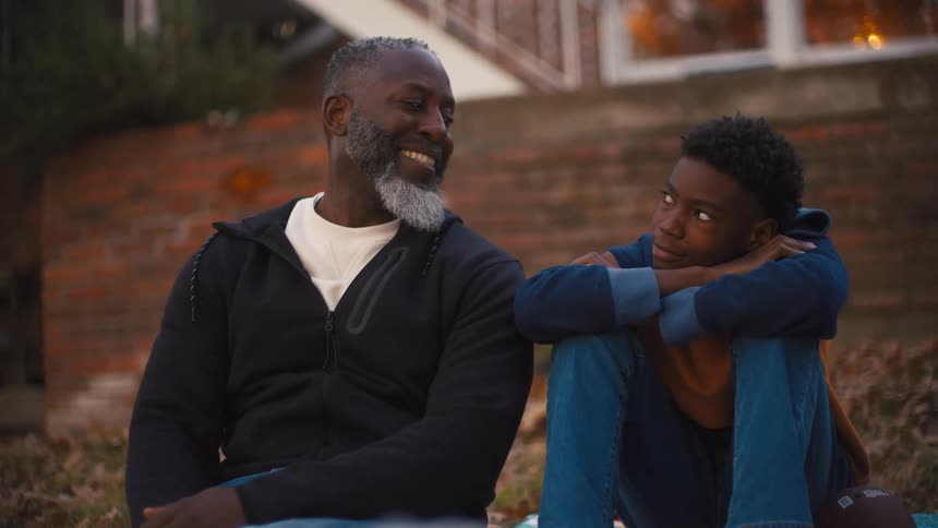 A man and his son are sitting on some steps and smiling at each other