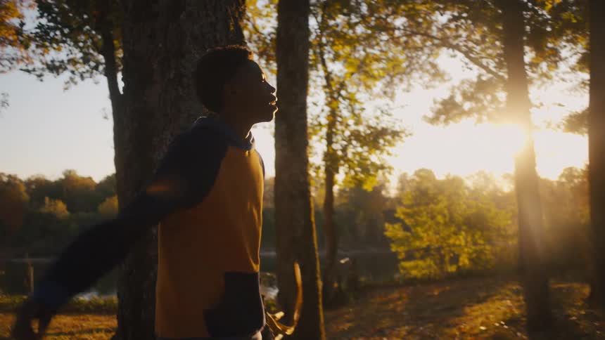Older man and woman play football with teens in woods near river and house