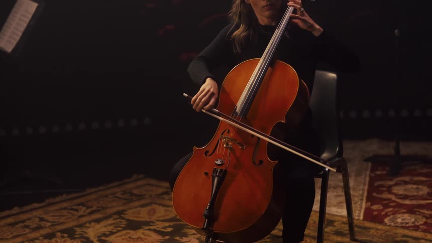 A woman is sitting in a chair holding a bow and playing the cello