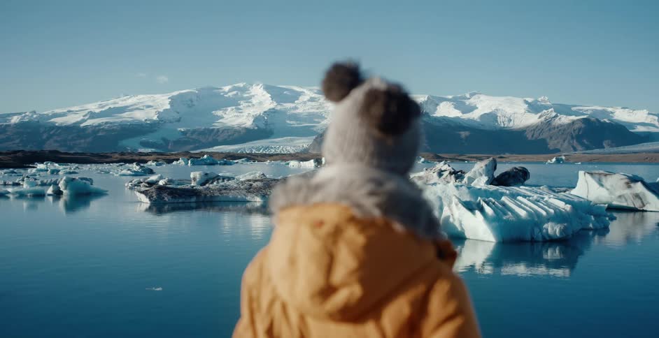 A woman in a winter hat and coat looking at a lake with snow and ice