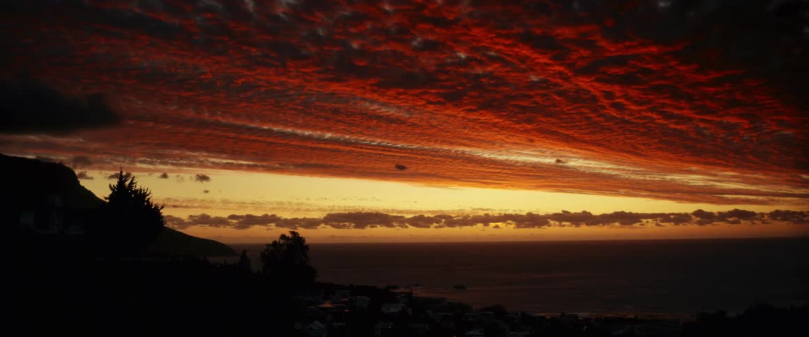 The sun sets and crimson clouds and the landscape near costal town turn black