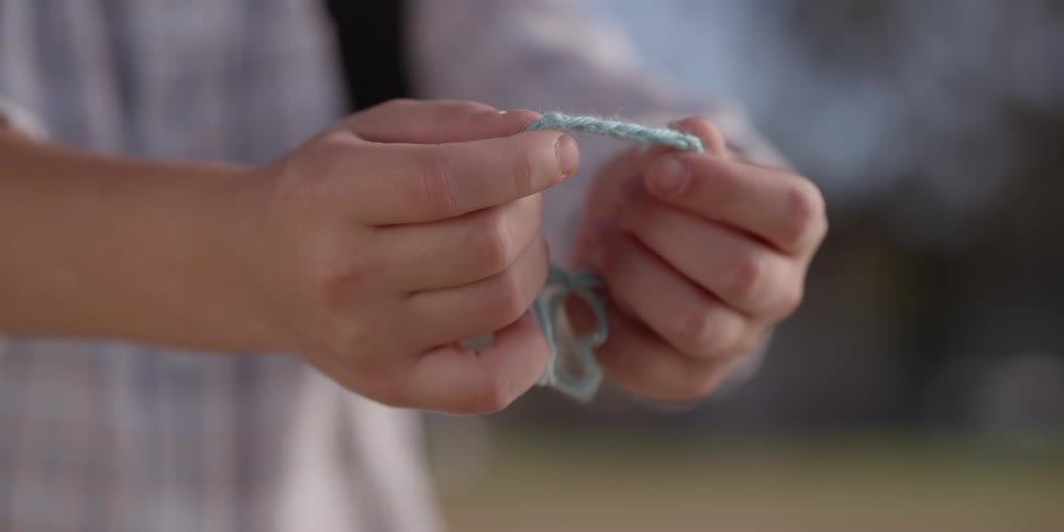 Person standing outdoors holds out bracelet made from yarn