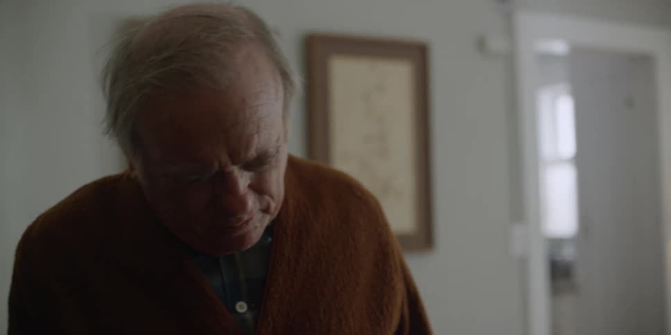 An elderly man is walking inside of his home