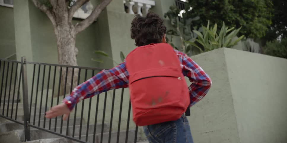 A young boy wearing a backpack runs up stairs outside of a home