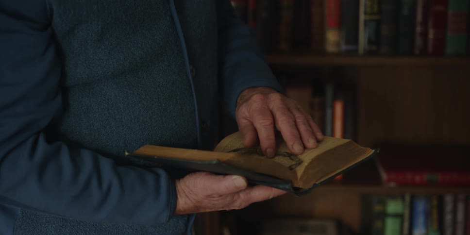 An elderly man removing a book from a bookshelf at home