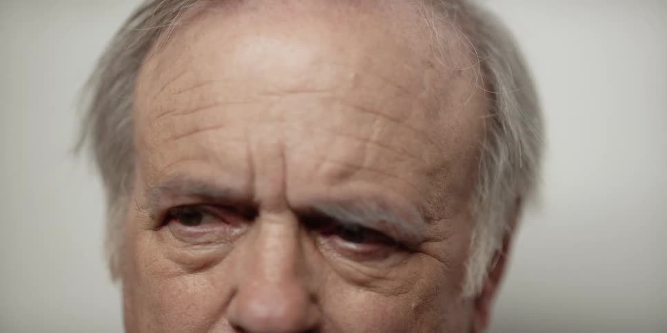 A man squints his eyes while standing in front of a white wall
