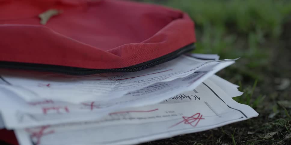 A red backpack with graded assignments lying on a grassy lawn