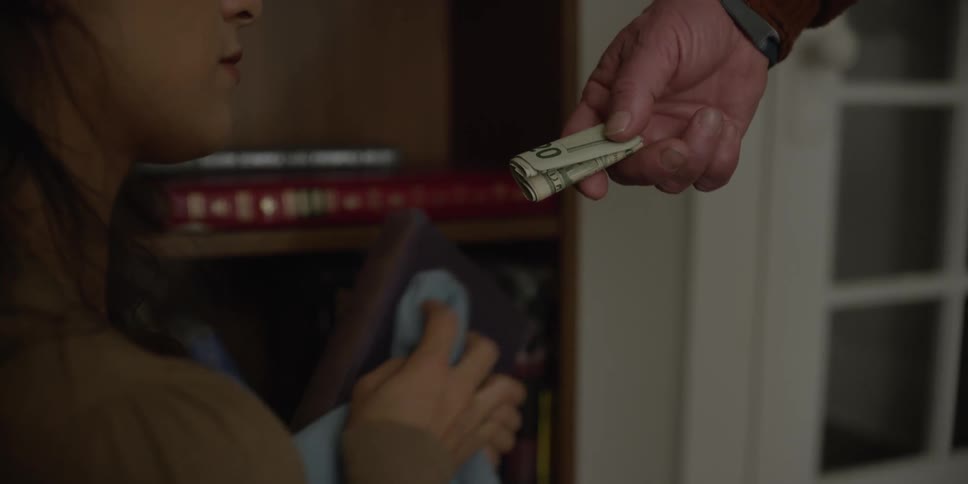A man offering cash to a woman cleaning a bookshelf