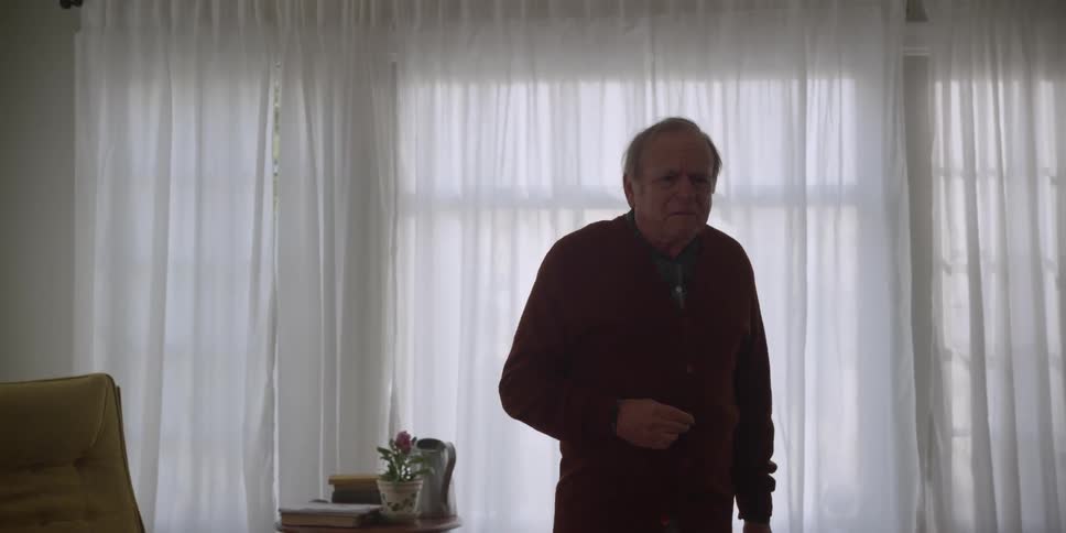 A man is standing in his living room thinking and then he walks across the room