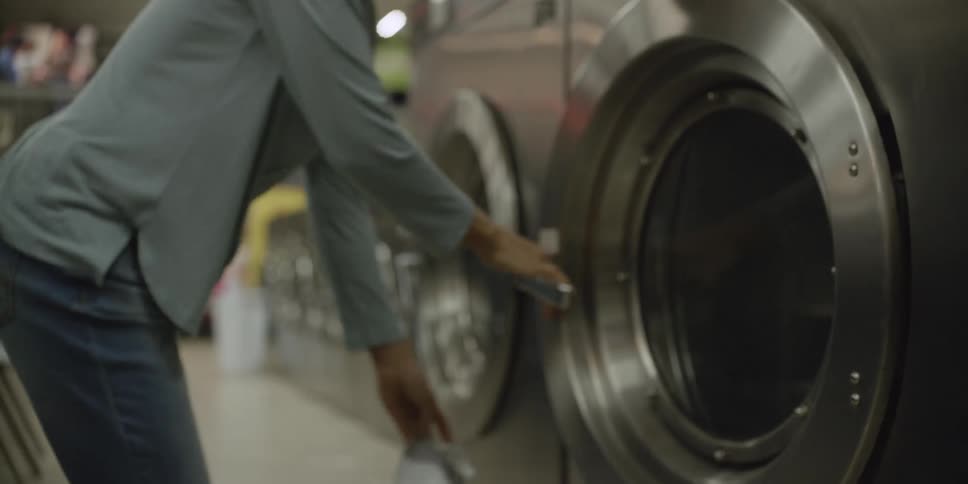 Woman with light blue shirt and jeans opens washing machine door at laundry