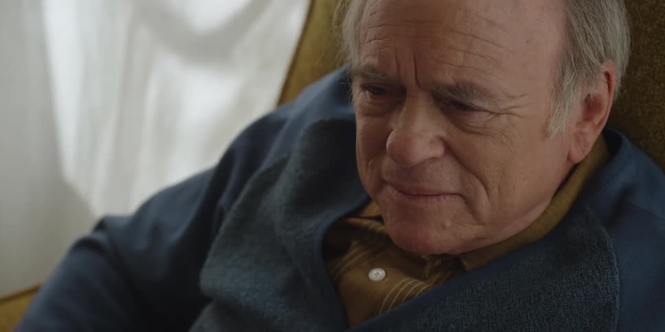 An elderly man sits in a chair and looks around a room