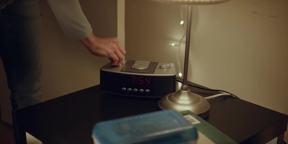 Man adjusts dial on clock radio sitting on table near lamp