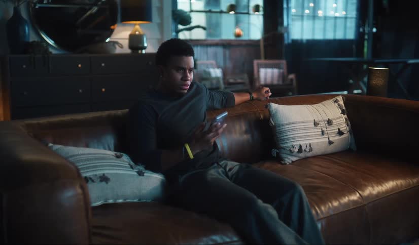 A man using a smartphone while watching television from a leather sofa