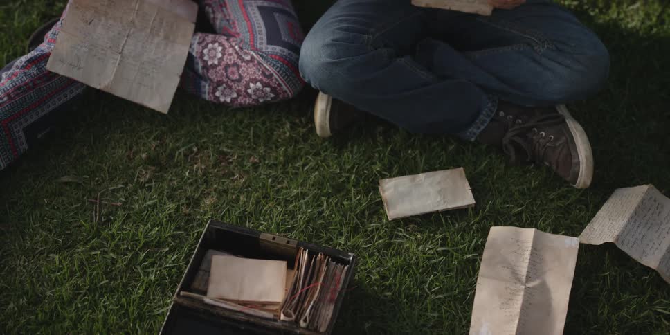 A man and woman sit outside and read from a box of handwritten letters