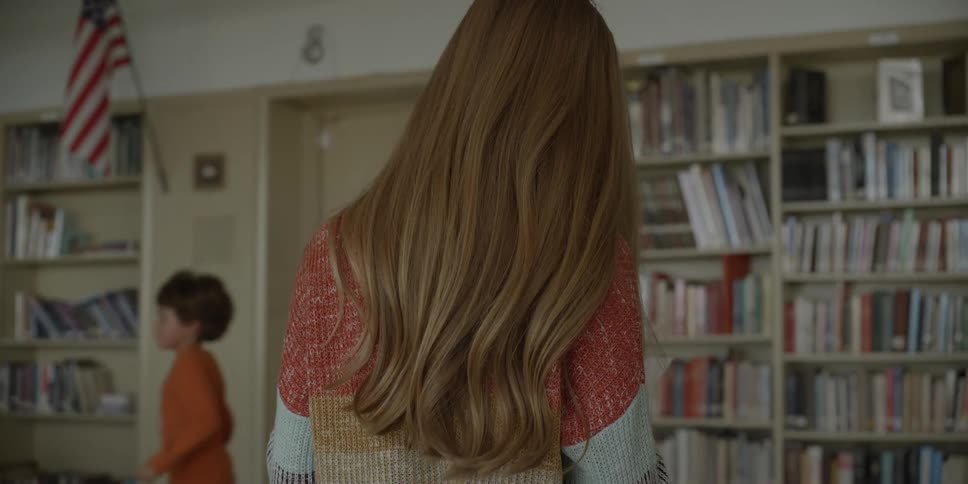 A female teacher reading a document in a school library with children in the background