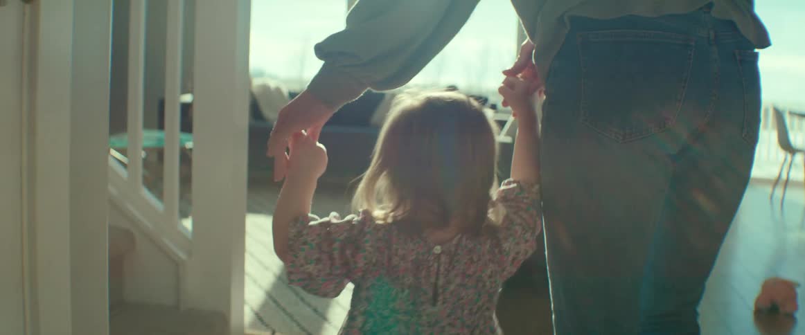 Mom holds both of her daughters hands as she helps her walk toward the sunny family room
