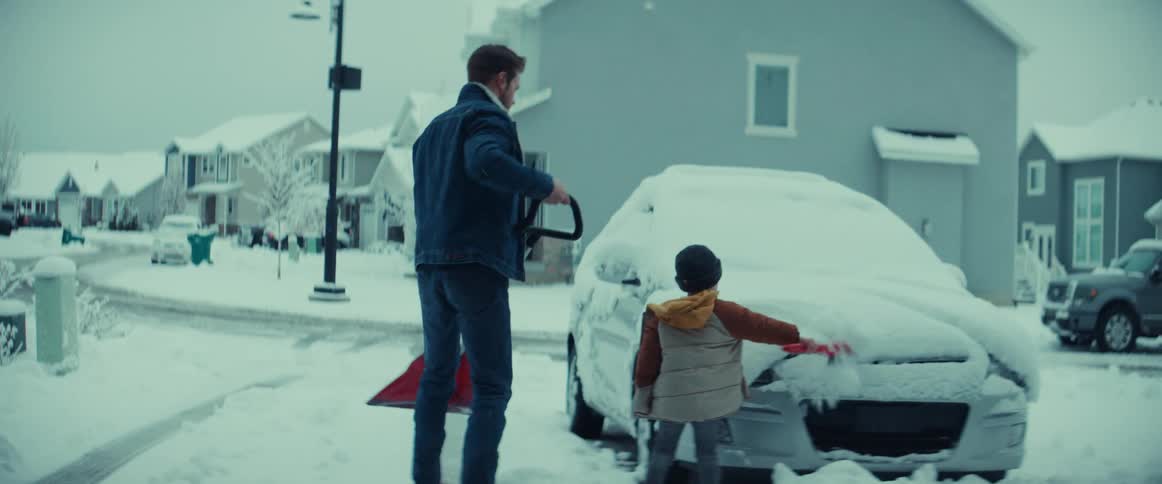 A father and young son clearing snow from a parked car after a winter storm