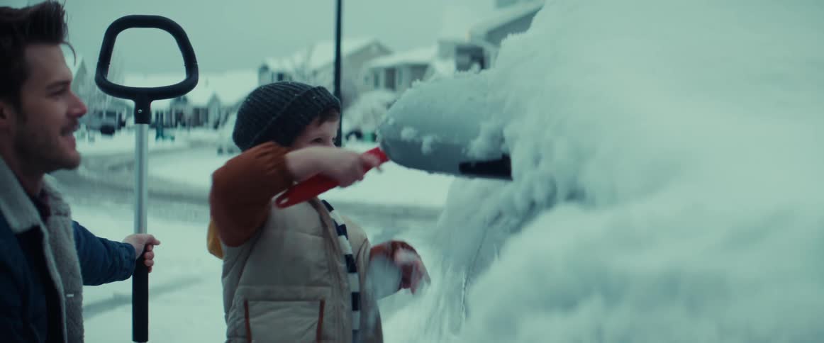 A father and young son wiping snow off a car after a winter storm