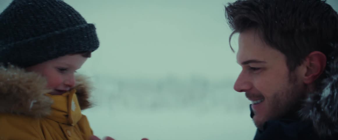 Man in snow with young son rubbing hands to get warm