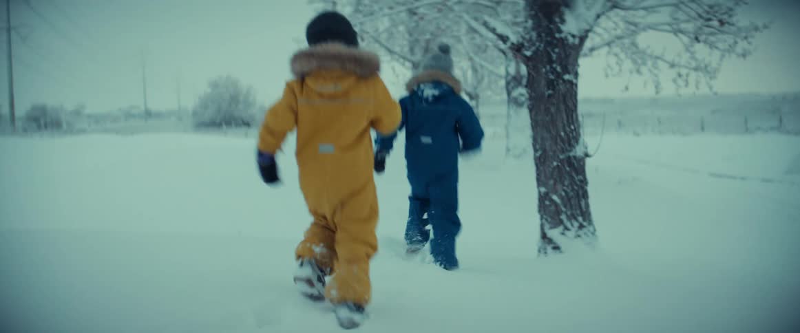 Children chase each other through the snow as an adult stands nearby