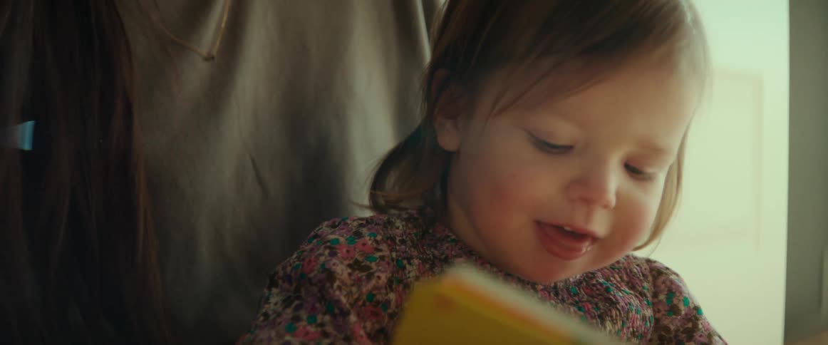 Mother strokes daughters hair as toddler looks at book