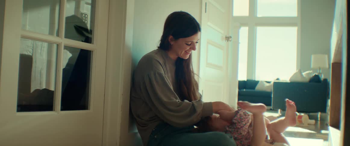A mother smiling and playing with her baby while sitting on the floor at home