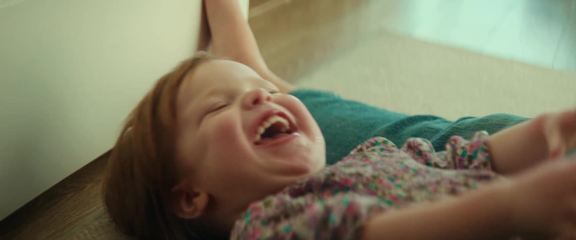 A mother is playing with her daughter on the floor as the little girl laughs