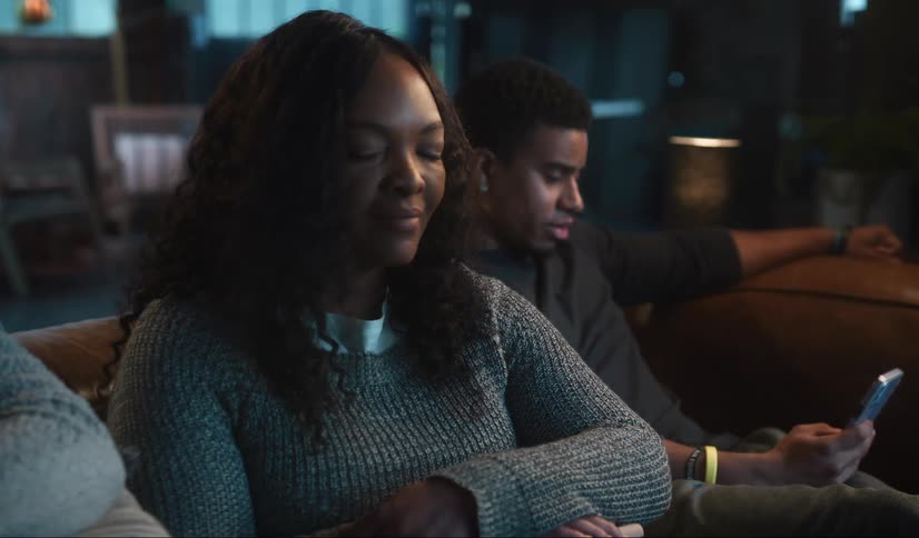 A woman is sitting down watching television with her teenage children and she sees they are both on their phones when she puts her phone down