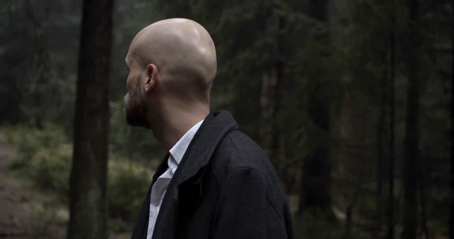 A man gazes into the distance before turning and walking along a forest path