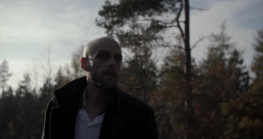 A man is standing outside in the shade looking around