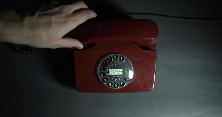 A male hand places the handset down on a rotary landline phone