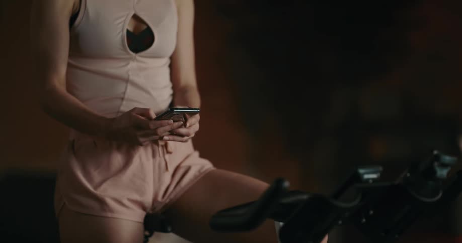 A woman is sitting on an exercise bike using her phone