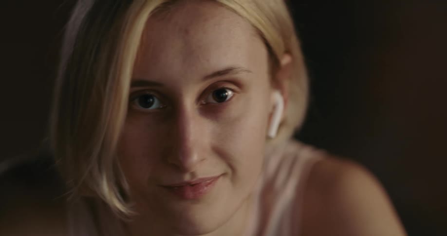 Light shines on the face of a young woman with brown eyes and short blond hair as she moves back and forth