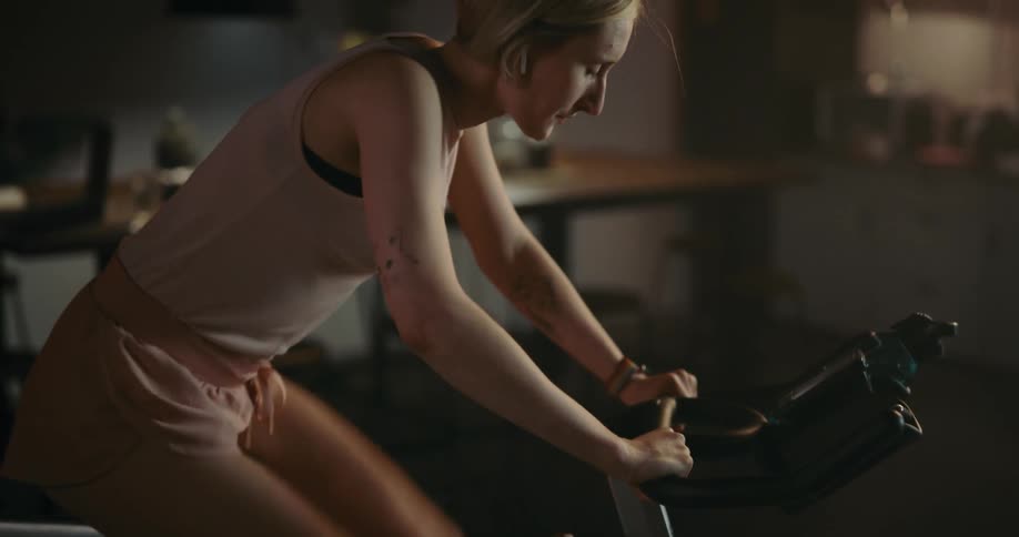 A woman with short blond hair is riding an exercise bike as she holds on tight and pedals fast